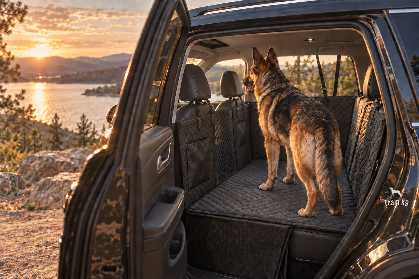 German shepherd standing on the Team K9 hard bottom seat cover in an SUV parked above a lake at sunset