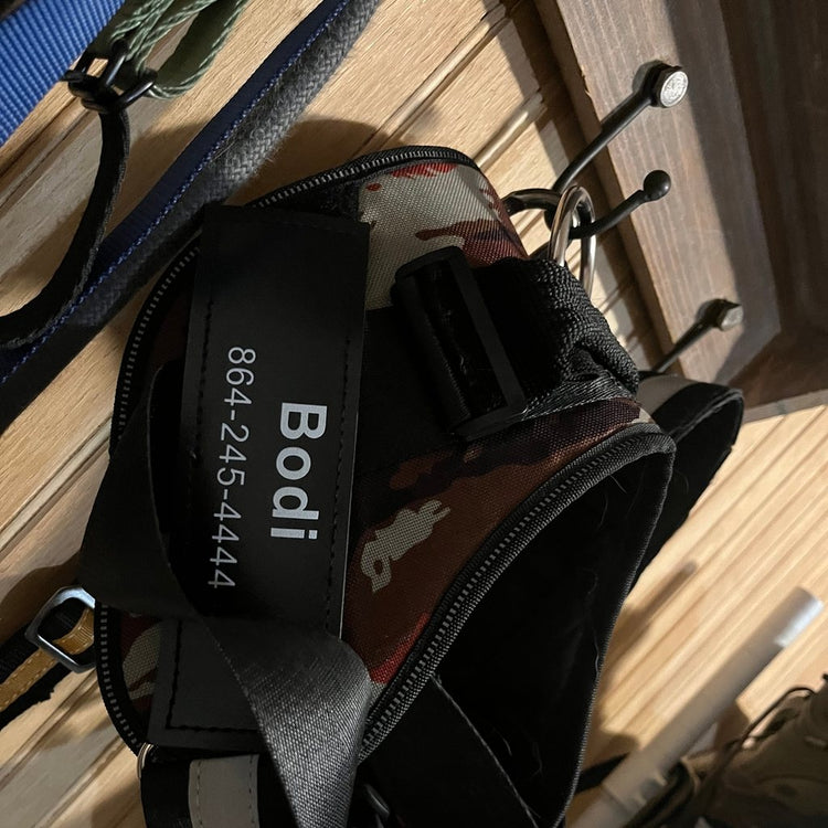 Custom name patch reading Bodi with a phone number on a black harness