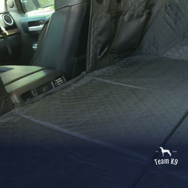 The black Team K9 hard bottom seat cover installed across a truck's back seat, its flat quilted floor bridging the footwell